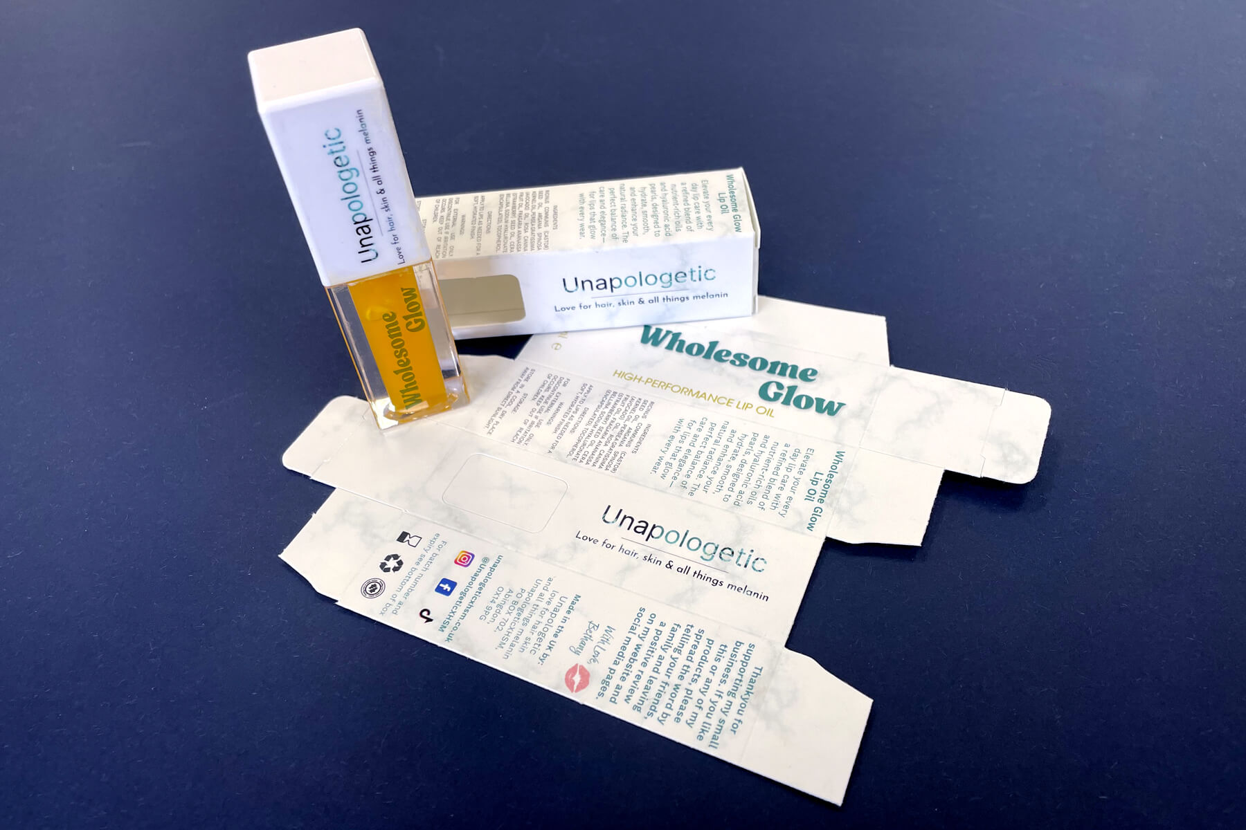 Wholesome Glow lip oil with product box on blue background