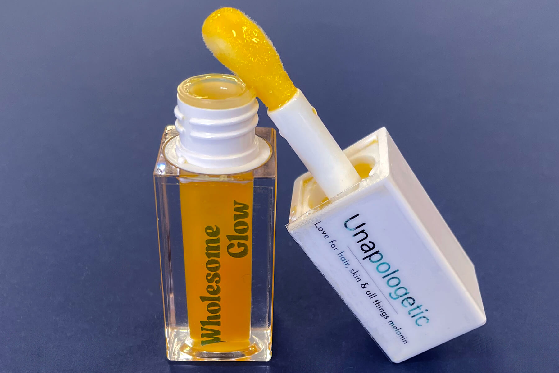 Bottle of Wholesome Glow lip oil on blue background